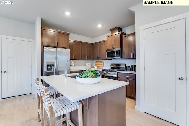 kitchen with stainless steel appliances, a sink, a breakfast bar area, light wood finished floors, and light countertops