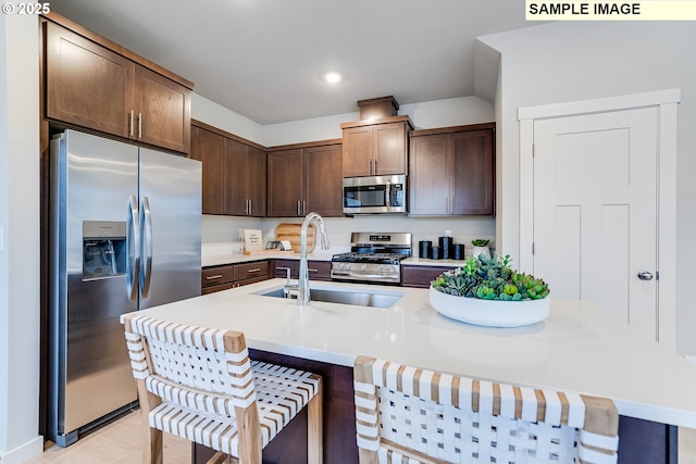 kitchen featuring stainless steel appliances, a sink, dark brown cabinets, a kitchen bar, and recessed lighting