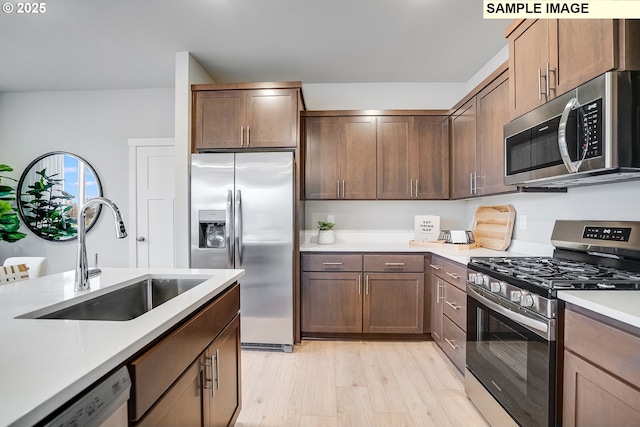 kitchen featuring appliances with stainless steel finishes, a sink, light countertops, and light wood-style flooring