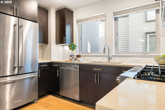 kitchen with tasteful backsplash, light countertops, light wood-style flooring, stainless steel appliances, and a sink