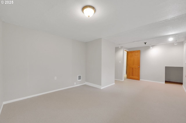 carpeted empty room featuring a textured ceiling and track lighting