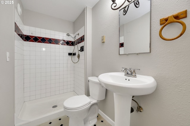 bathroom with toilet, tiled shower, and sink