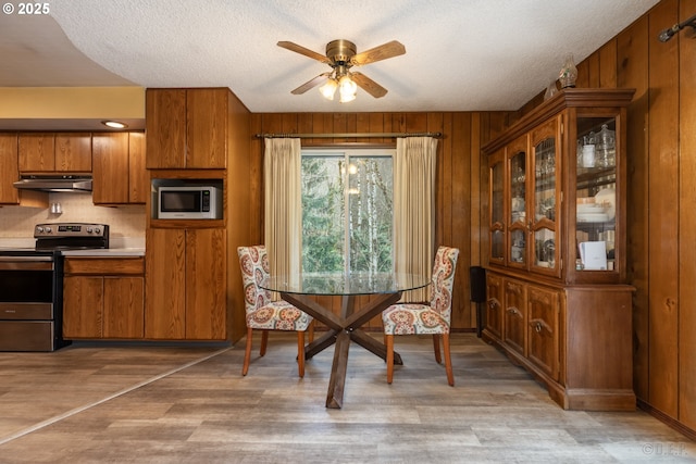 dining room with a ceiling fan, wood walls, light wood-style flooring, and a textured ceiling