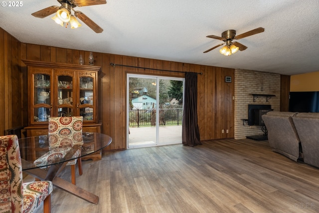 living area featuring a brick fireplace, ceiling fan, a textured ceiling, and wood finished floors