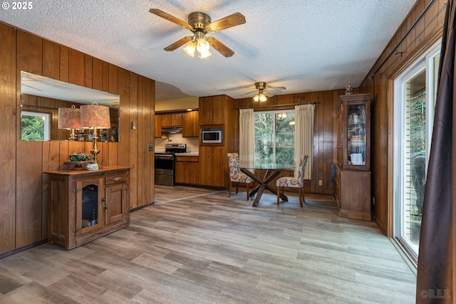 kitchen featuring stainless steel appliances, light countertops, brown cabinetry, plenty of natural light, and under cabinet range hood