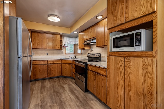 kitchen with stainless steel appliances, brown cabinetry, light countertops, and under cabinet range hood