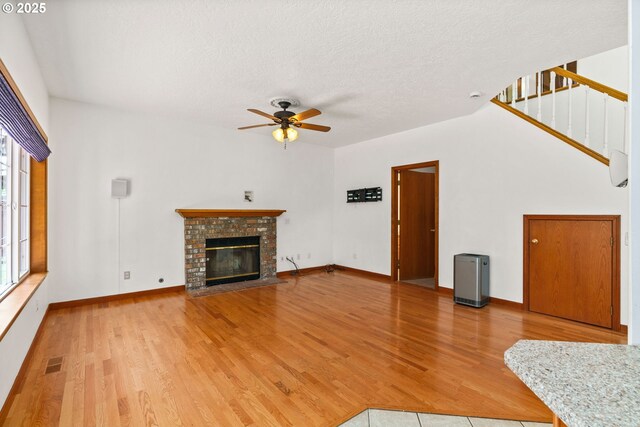 4060 Hampshire Ln, Eugene, OR 97404 - unfurnished living room featuring ceiling fan, light wood-style flooring, a brick fireplace, stairs, and a textured ceiling