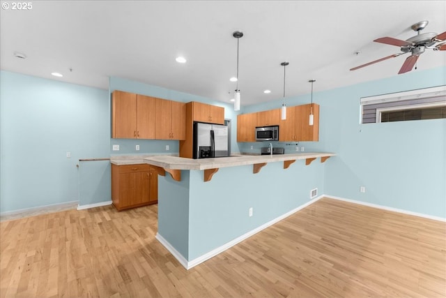 kitchen with appliances with stainless steel finishes, decorative light fixtures, a kitchen bar, kitchen peninsula, and light hardwood / wood-style flooring