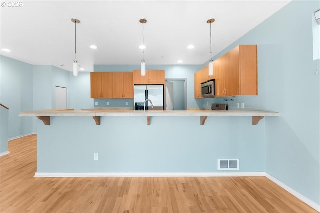 kitchen with a breakfast bar, pendant lighting, appliances with stainless steel finishes, and kitchen peninsula