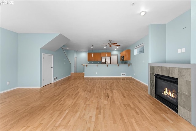 unfurnished living room with light hardwood / wood-style floors, a tile fireplace, and ceiling fan