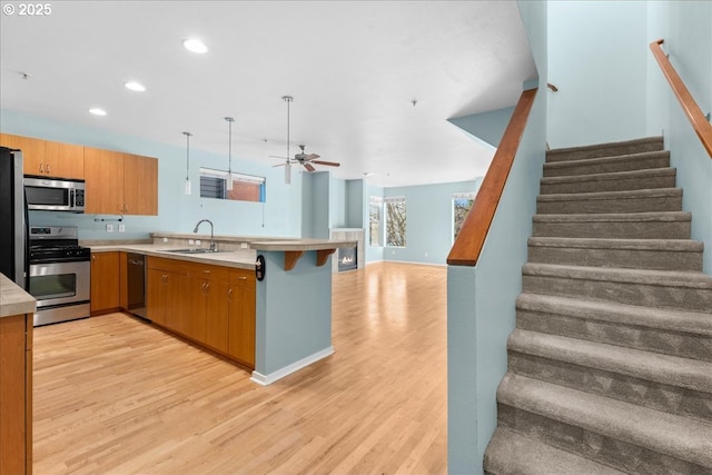 kitchen featuring pendant lighting, appliances with stainless steel finishes, sink, kitchen peninsula, and light hardwood / wood-style flooring