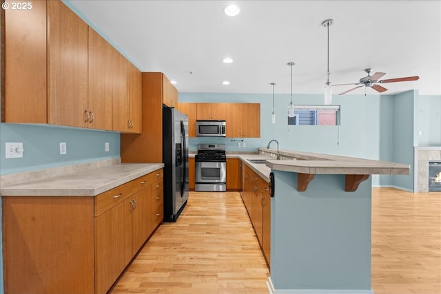 kitchen featuring a breakfast bar area, stainless steel appliances, decorative light fixtures, light wood-type flooring, and sink