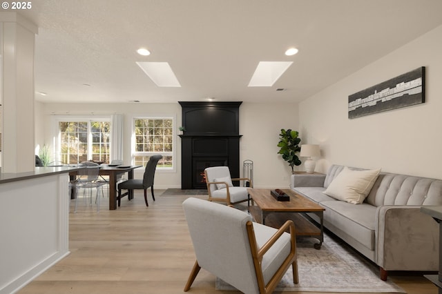 living area with baseboards, a skylight, recessed lighting, a fireplace, and light wood-style floors