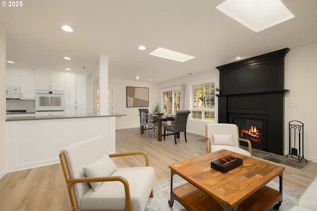 living room with light wood finished floors, recessed lighting, a fireplace, and a skylight