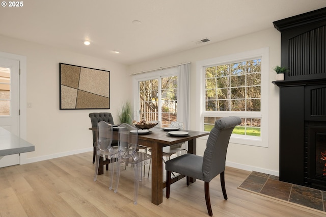 dining room with visible vents, baseboards, a fireplace with flush hearth, and wood finished floors