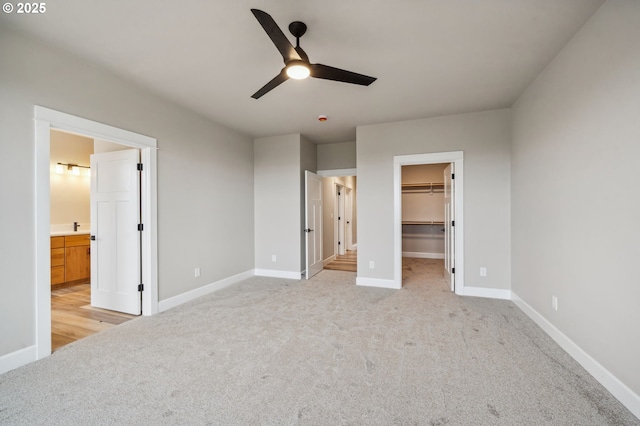 unfurnished bedroom with a spacious closet, light colored carpet, a closet, and ceiling fan