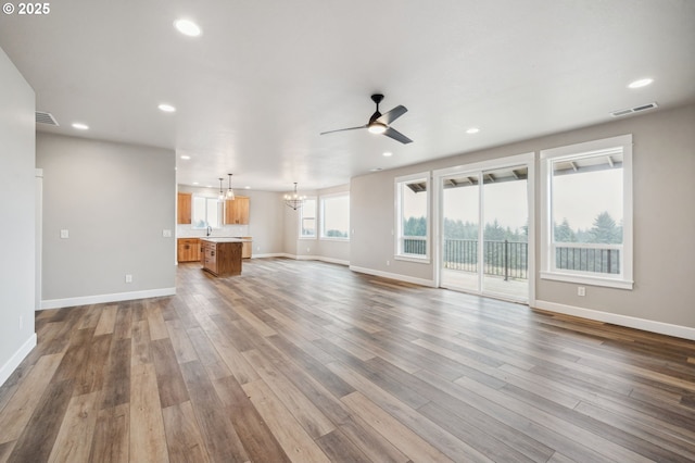 unfurnished living room with hardwood / wood-style floors, ceiling fan with notable chandelier, and sink