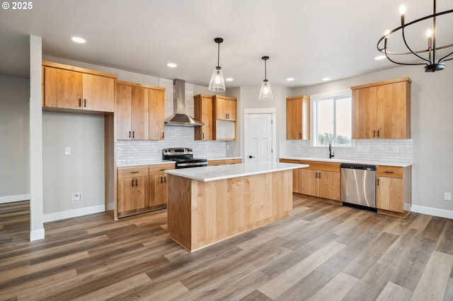 kitchen featuring a kitchen island, hanging light fixtures, stainless steel appliances, wall chimney range hood, and light hardwood / wood-style flooring