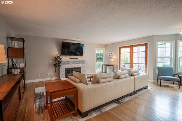 living area featuring wood finished floors, baseboards, french doors, a textured ceiling, and a glass covered fireplace