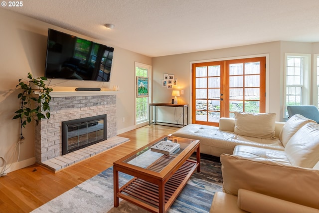 living room featuring plenty of natural light, a brick fireplace, french doors, and wood finished floors