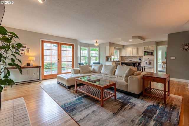 living area featuring light wood finished floors, french doors, a textured ceiling, and baseboards