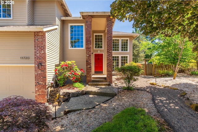 property entrance featuring a garage, brick siding, and fence