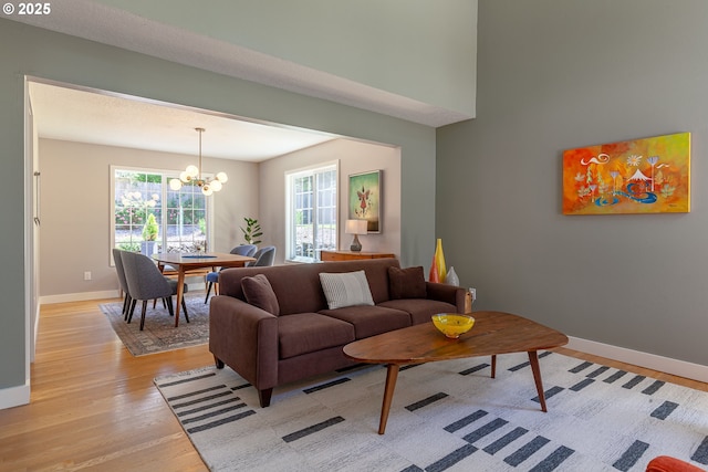 living room with a chandelier, baseboards, and light wood-style floors