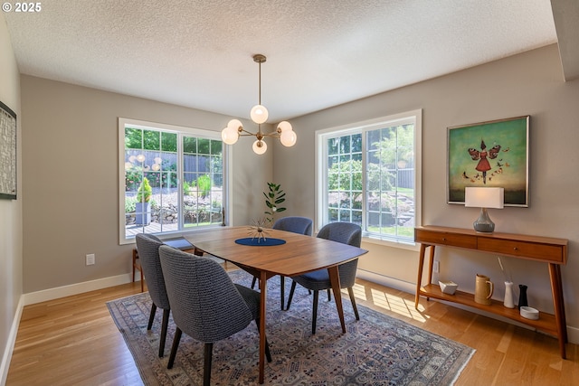 dining space with an inviting chandelier, baseboards, light wood finished floors, and a textured ceiling