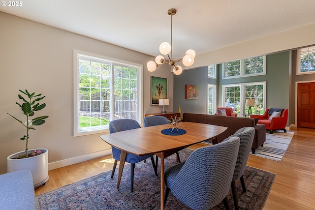 dining space featuring a chandelier, a textured ceiling, baseboards, and light wood-style floors