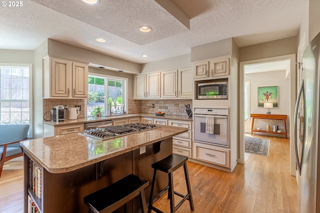 kitchen with a center island, appliances with stainless steel finishes, a breakfast bar area, light wood finished floors, and decorative backsplash