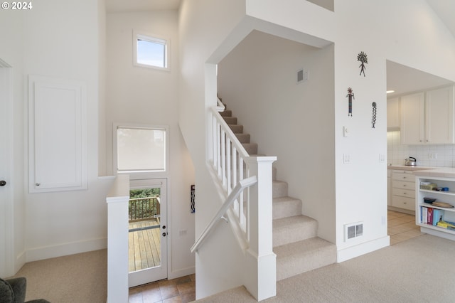 staircase featuring visible vents, a towering ceiling, tile patterned flooring, carpet floors, and baseboards
