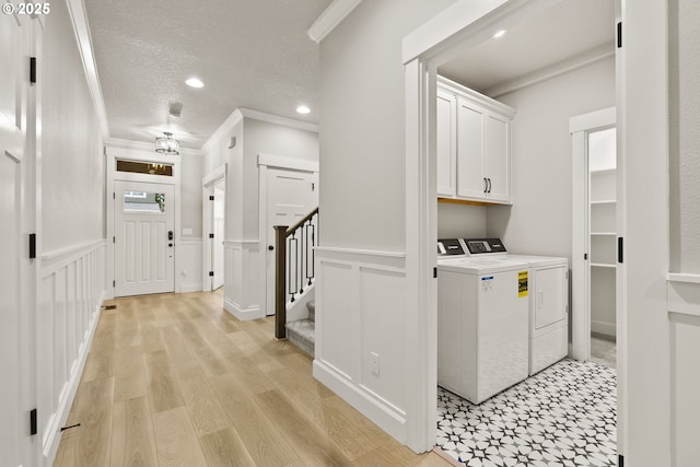 washroom featuring a textured ceiling, light wood-style floors, wainscoting, washer and clothes dryer, and crown molding