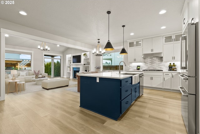 kitchen with white cabinetry, open floor plan, light countertops, an island with sink, and glass insert cabinets