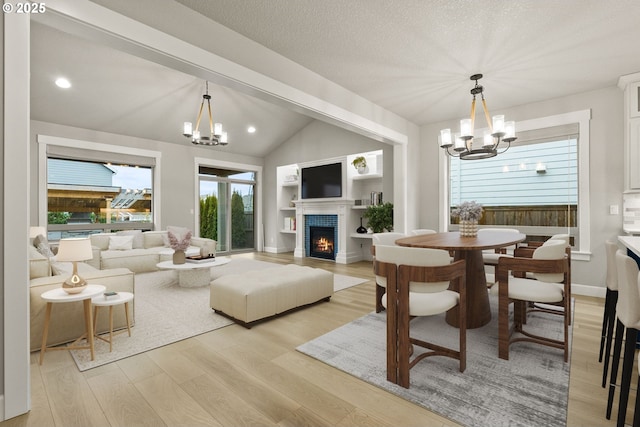 living room featuring lofted ceiling, light wood-style floors, a warm lit fireplace, and a notable chandelier