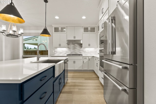 kitchen featuring blue cabinets, stainless steel appliances, white cabinets, light countertops, and glass insert cabinets