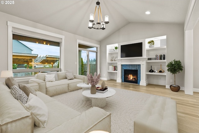 living room with lofted ceiling, a notable chandelier, a tile fireplace, and light wood-style floors