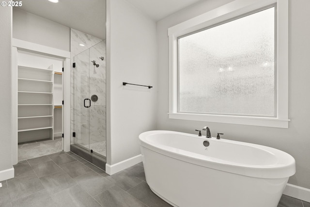 full bathroom featuring a shower stall, a spacious closet, baseboards, and a freestanding bath