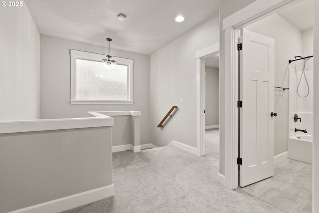 hallway with baseboards, light colored carpet, a textured ceiling, and an upstairs landing