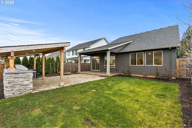 rear view of house with roof with shingles, a patio, a lawn, fence, and exterior kitchen