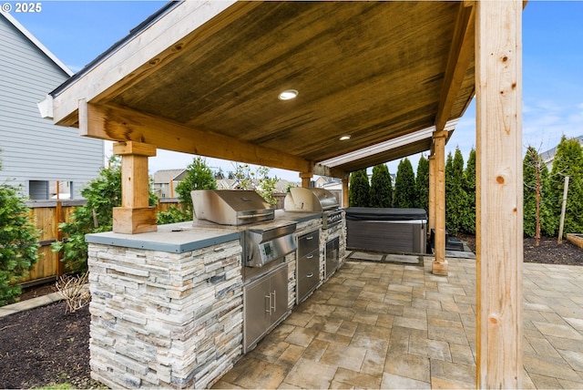 view of patio with a hot tub, fence, grilling area, and exterior kitchen