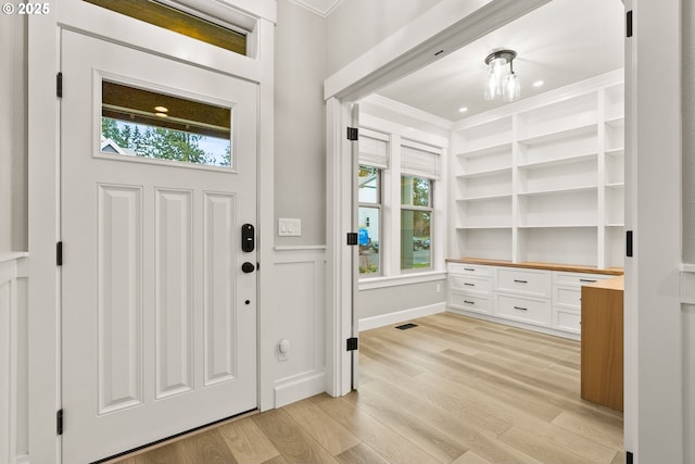 entrance foyer featuring visible vents, light wood finished floors, ornamental molding, and built in desk