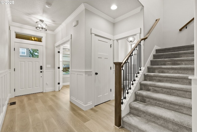 entryway with visible vents, wainscoting, stairs, crown molding, and light wood-type flooring