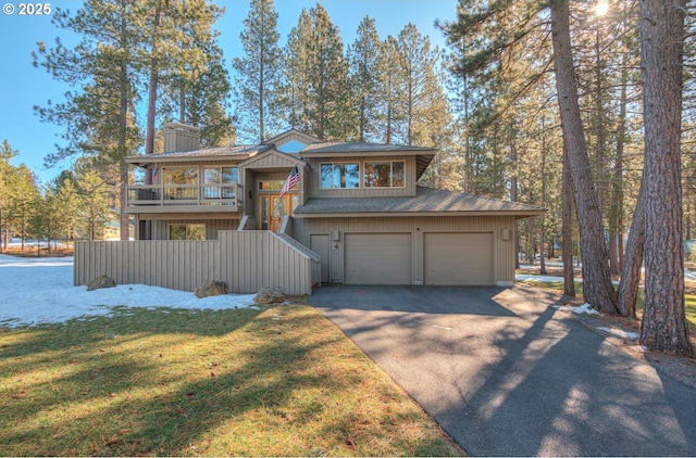 chalet / cabin featuring a shingled roof, aphalt driveway, a front yard, a chimney, and a garage