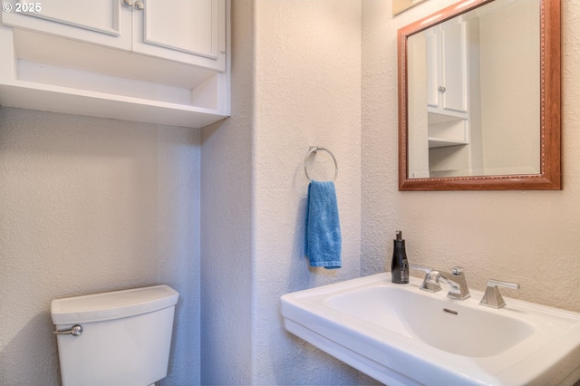 bathroom with toilet, a textured wall, and a sink