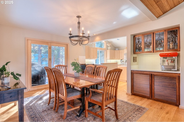 dining room with a wealth of natural light, light wood-type flooring, a notable chandelier, and vaulted ceiling