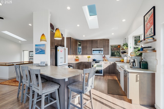 9065 8th St, Bay City, OR 97107 - kitchen with appliances with stainless steel finishes, a skylight, a peninsula, dark brown cabinets, and a kitchen bar