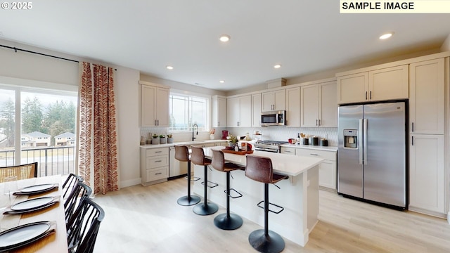 kitchen featuring appliances with stainless steel finishes, a kitchen bar, light countertops, decorative backsplash, and recessed lighting