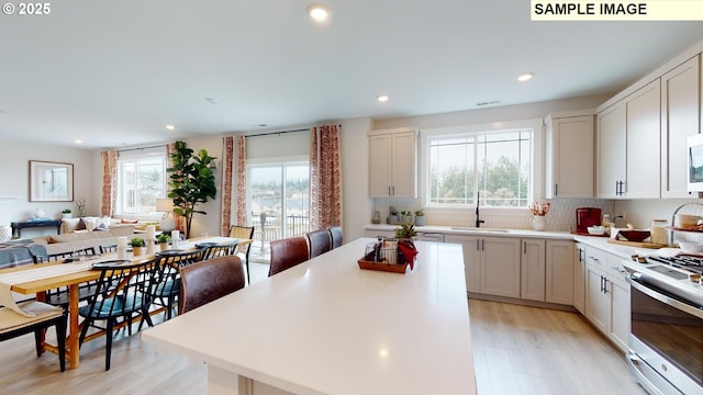 kitchen with stainless steel range with gas cooktop, light wood-type flooring, a sink, recessed lighting, and light countertops