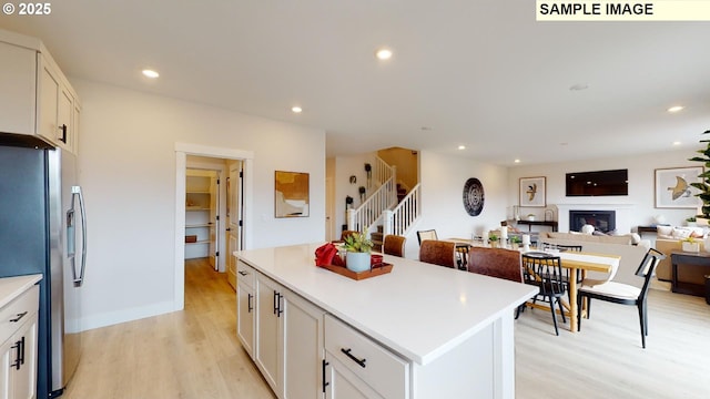 kitchen featuring stainless steel fridge, light wood-type flooring, white cabinetry, light countertops, and recessed lighting