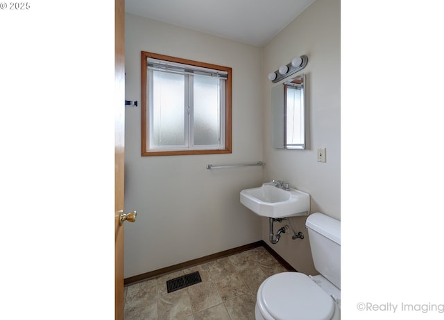 half bathroom featuring toilet, baseboards, visible vents, and a sink